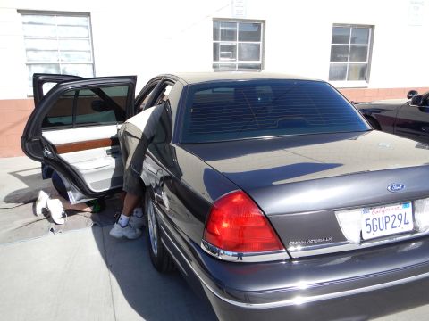 2003 Ford Crown Victoria - dark gray Ford Crown Victoria LX sedan with California plate 5GUP294 sits with a rear door open as someone works at the door sill.