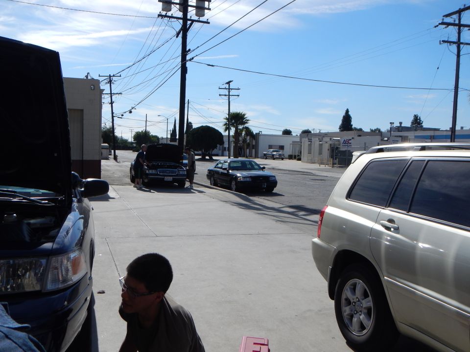 Street view with a tan Toyota SUV, a black sedan and other cars along an industrial road under power lines