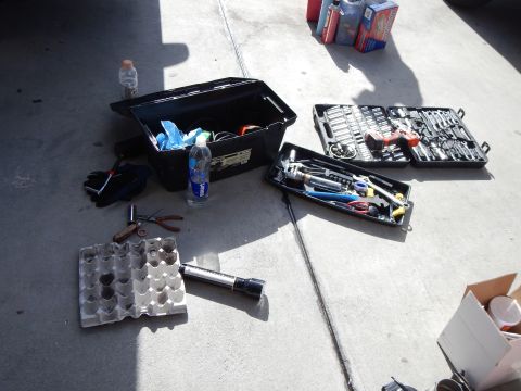 2003 Ford Crown Victoria - open black toolbox, a socket set, hand tools and a bottle of water are spread across a sunlit concrete floor.