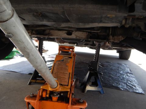 2003 Ford Crown Victoria - View beneath a vehicle raised on an orange Pro Series floor jack and a jack stand, with exhaust and suspension visible over a tarp.