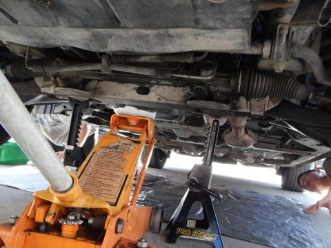 2003 Ford Crown Victoria - underbody of a car raised on an orange jack and stand reveals the steering rack and exhaust as a person reaches in from the side.