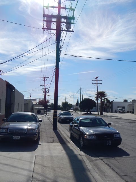 2003 Ford Crown Victoria - Gray and black Ford Crown Victoria sedans line an industrial street beneath a utility pole against a bright cloudy sky.