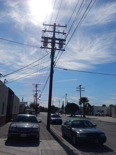 2003 Ford Crown Victoria - wooden power pole and transmission lines tower over an industrial street with two dark sedans parked along the curb.
