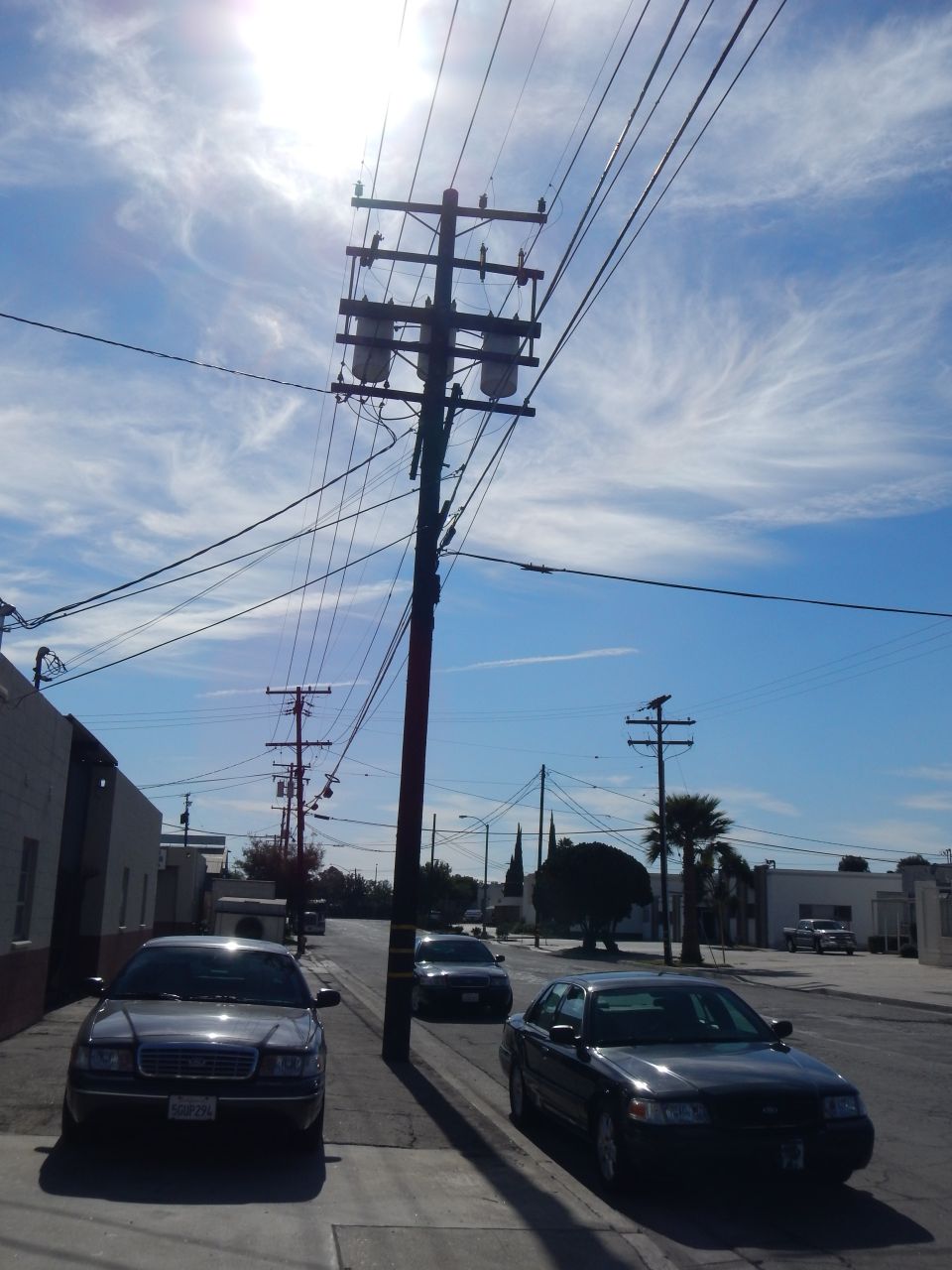 Backlit utility pole over an industrial street with two dark sedans parked below