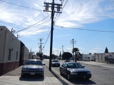 2003 Ford Crown Victoria - dark Ford sedan and a black sedan parked along an industrial street beside warehouse buildings under utility lines.
