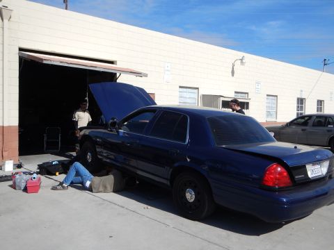 2003 Ford Crown Victoria - dark blue Ford Crown Victoria sedan with its hood up parked outside a shop, with two people attending to it.
