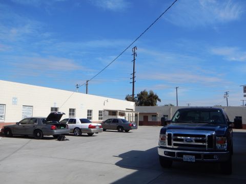 2003 Ford Crown Victoria - paved lot holding several silver Ford sedans and a dark blue Ford pickup parked along a long white industrial building.