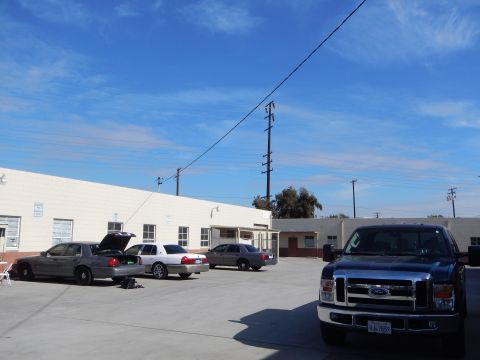 2003 Ford Crown Victoria - Several silver Ford sedans, one with hood and trunk open, parked with a dark blue Ford pickup in a wide paved lot.