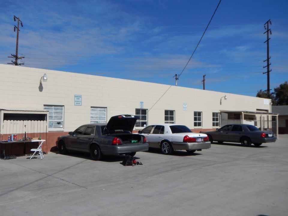 Three gray and silver Ford sedans parked at a beige industrial building