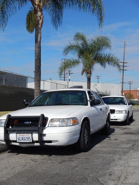 2003 Ford Crown Victoria - white Ford Crown Victoria with a front push bar parked under palm trees at a curb, with another white sedan behind it.