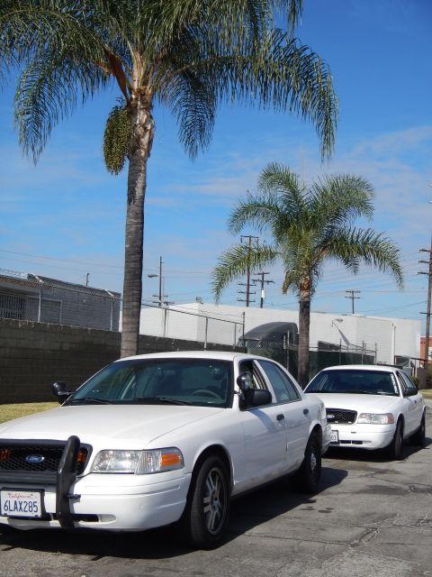 2003 Ford Crown Victoria - white Ford Crown Victoria with front push bar parked under palm trees at a curb, a second white sedan parked behind it.