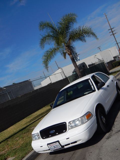 2003 Ford Crown Victoria - white Ford Crown Victoria sedan photographed from a low front angle beside a tall palm tree on a sunny day.