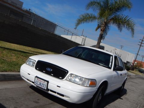 2003 Ford Crown Victoria - Front three-quarter view of a white Ford Crown Victoria sedan parked near palm trees beside an industrial building.