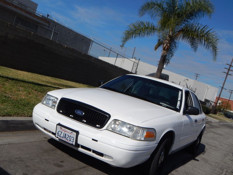 White Ford Crown Victoria sedan front three-quarter view by palm trees