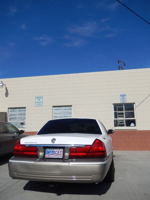 2003 Ford Crown Victoria - Straight rear view of a white-over-tan Mercury Grand Marquis sedan parked behind a tan building under a deep blue sky.