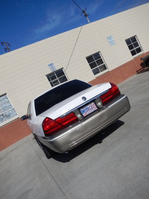 2003 Ford Crown Victoria - Low rear angle of a white-over-tan Mercury Grand Marquis sedan parked beside a tan building with windows.