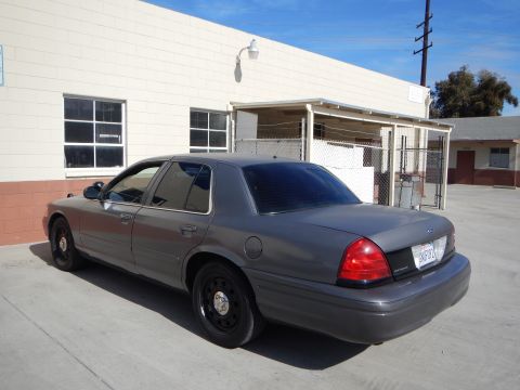2003 Ford Crown Victoria - Rear-quarter view of a gray Ford Crown Victoria sedan with black steel wheels and tinted windows parked by a building.