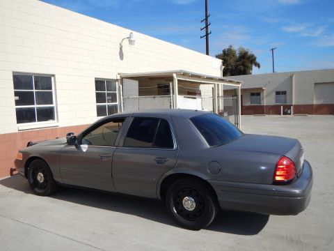 2003 Ford Crown Victoria - Side profile of a gray Ford Crown Victoria sedan with black steel wheels and tinted windows parked beside a building.