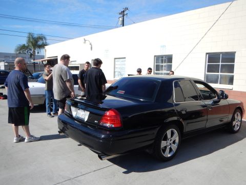2003 Ford Crown Victoria - group of men stand around a black Mercury Marauder sedan with chrome wheels parked outside an auto shop.