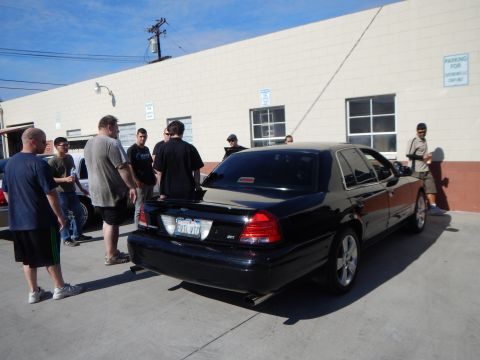2003 Ford Crown Victoria - Rear view of a black Mercury Marauder sedan with chrome wheels as a group of men stand talking beside it.