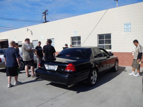 2003 Ford Crown Victoria - Rear-quarter view of a black Mercury Marauder sedan parked outside a shop with several people gathered around it.