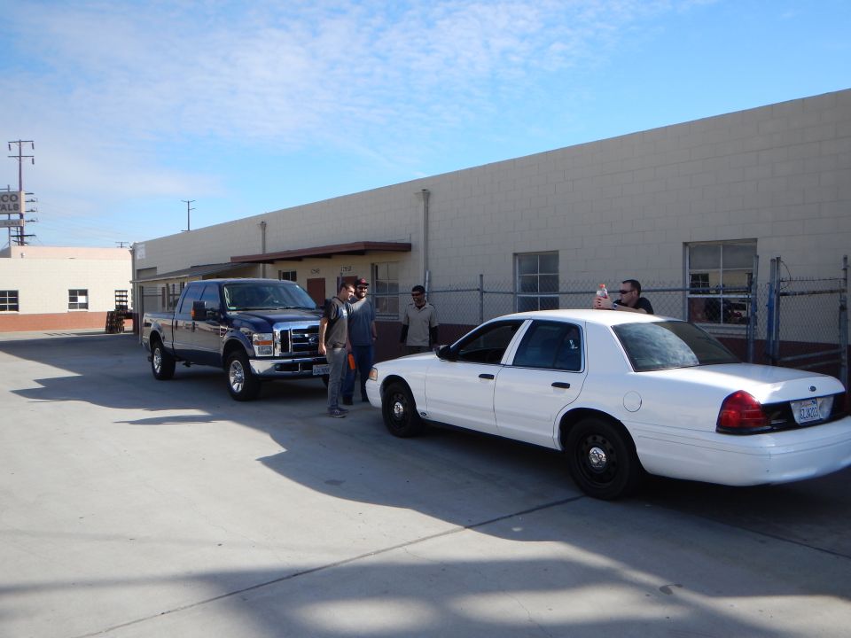 Dark Ford pickup truck and white Crown Victoria sedan by a building