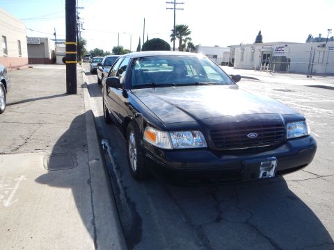 2003 Ford Crown Victoria - black Ford sedan fitted with a hood deflector and bearing the Ford grille emblem sits at a curb beside an industrial building.