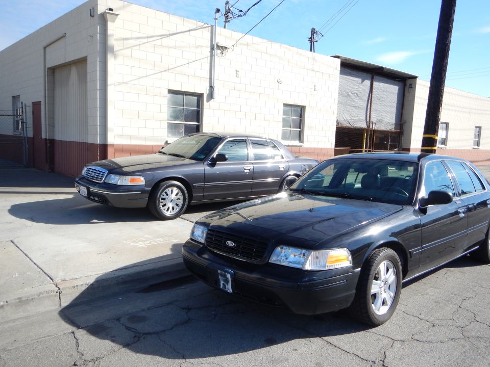 Two dark Ford sedans parked outside a cinderblock industrial building