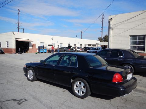 2003 Ford Crown Victoria - black Ford sedan seen from the rear three-quarter sits in a paved lot with more cars and a warehouse in the background.