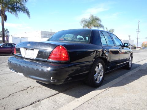 2003 Ford Crown Victoria - black Ford Crown Victoria sedan, viewed from the rear three-quarter, sits on cracked pavement with palm trees behind it.