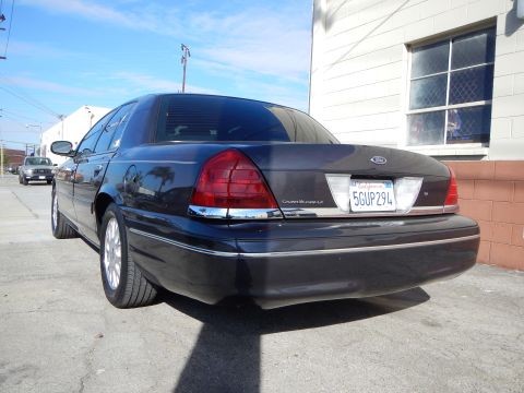2003 Ford Crown Victoria - dark blue Ford Crown Victoria LX sedan seen from the rear three-quarter, with plate 5GUP294 and a building behind it.