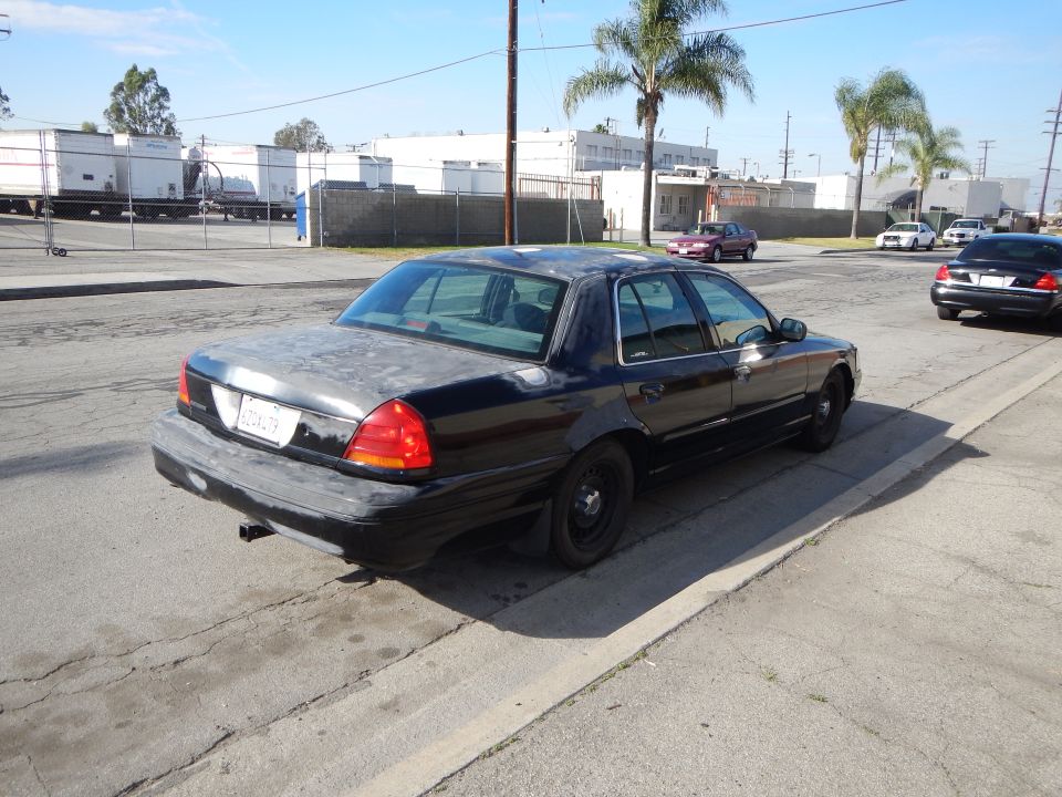 Rear three-quarter of a black Ford sedan with steel wheels at a curb
