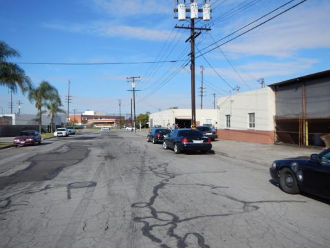 2003 Ford Crown Victoria - Several sedans line a cracked industrial street with power poles, a palm tree and white warehouse buildings under a blue sky.