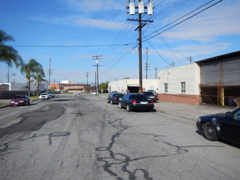 Industrial street with parked sedans, power lines and palm tree under blue sky