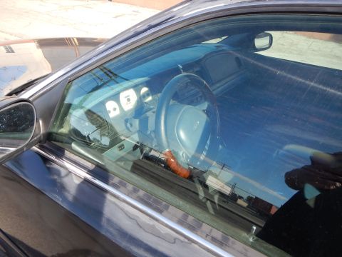 2003 Ford Crown Victoria - View through a side window into a sedan interior showing the steering wheel, dashboard gauges and a beverage bottle in the console.