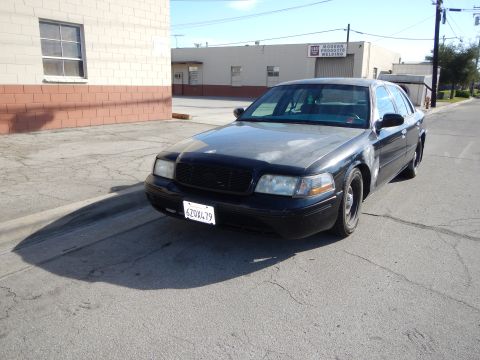 2003 Ford Crown Victoria - black Ford sedan parked in a lot beside cinderblock buildings, shown front three-quarter with a California license plate.