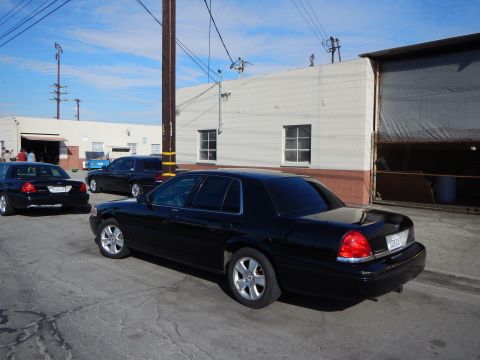 2003 Ford Crown Victoria - black full-size sedan shown rear three-quarter parked in an industrial lot near other dark sedans and a beige warehouse.