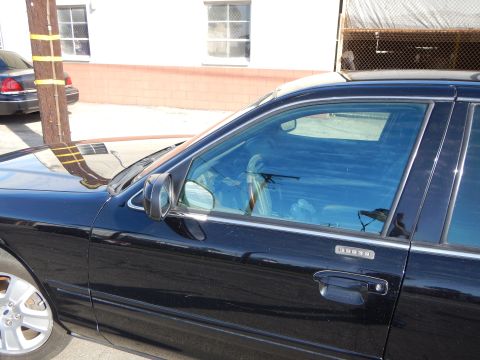 2003 Ford Crown Victoria - Close detail of a black sedan's front fender, side mirror and window with chrome rocker trim, parked beside a building.