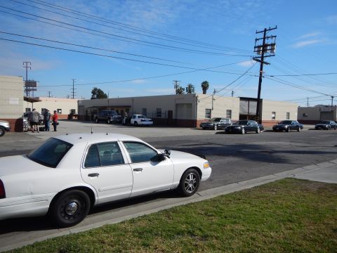 2003 Ford Crown Victoria - white sedan shown front three-quarter parked by a grass strip with several other cars and warehouses across the lot.