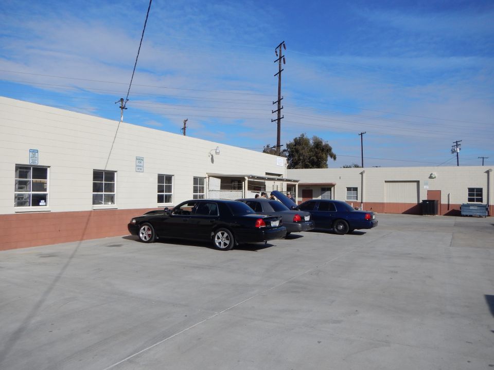 Three dark sedans parked in lot behind warehouse under blue sky