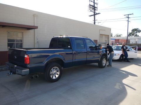 2003 Ford Crown Victoria - blue Ford crew-cab pickup parked beside a white sedan in a lot, with two people standing by the cars near a warehouse.