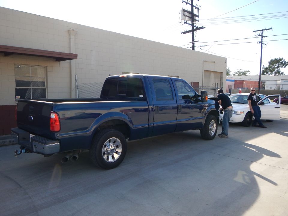 Blue Ford crew-cab pickup beside white sedan with people in lot