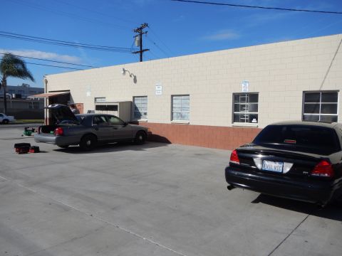 2003 Ford Crown Victoria - gray sedan with its trunk open and a black sedan parked in a concrete lot behind a beige warehouse with windows.