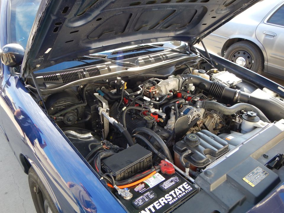 Engine bay of a blue car showing V8 engine and Interstate battery
