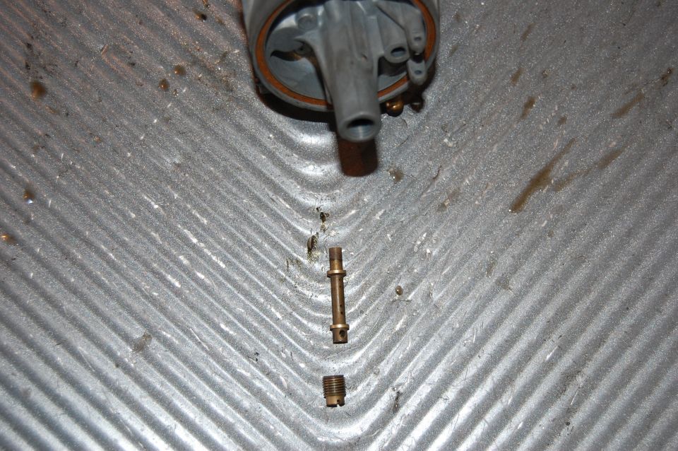 Disassembled carburetor with brass jet and threaded piece on a ribbed metal surface