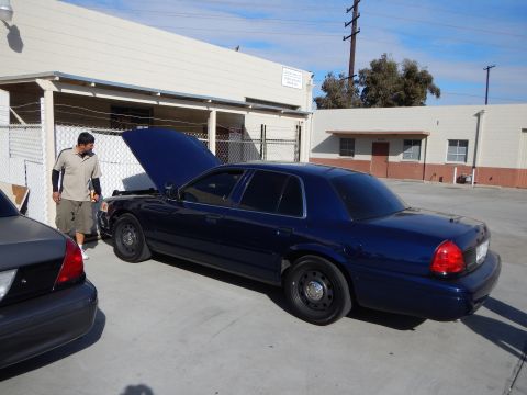 2003 Ford Crown Victoria - dark blue Ford Crown Victoria parked outside a tan building has its hood raised while a man stands at the front.