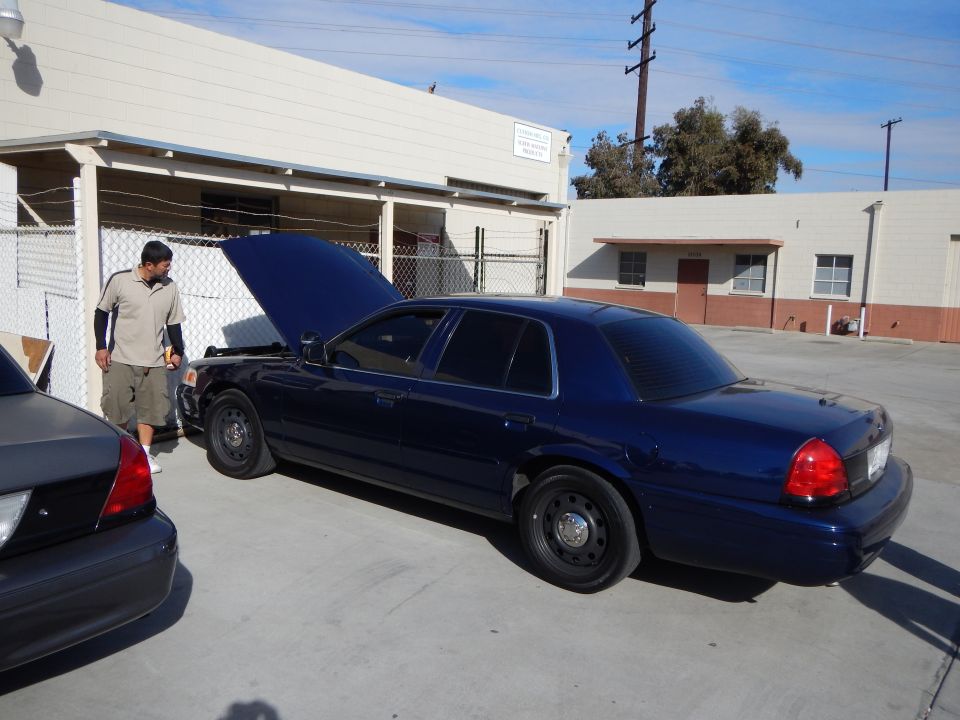 Side rear view of a dark blue Ford Crown Victoria with hood up in a shop lot
