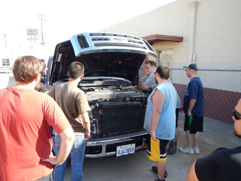 2003 Ford Crown Victoria - Men gather at the open front of a Ford pickup truck, looking at the exposed radiator and engine bay outside a shop.