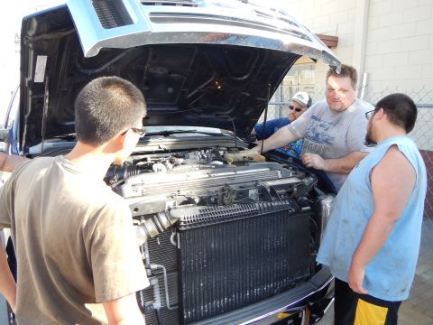 2003 Ford Crown Victoria - Several men lean over the open engine bay of a pickup truck, examining the radiator and engine components.