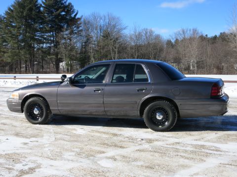 2001 Ford Crown Victoria - A gray 2001 Ford Crown Victoria sedan is parked on a snow-covered surface under a clear blue sky.